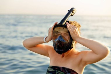 Plajda tropikal tatilin tadını çıkaran güzel bir bayan turist, deniz yaşamını keşfetmek için altın saat gün batımında şnorkel maskesi takıyor..