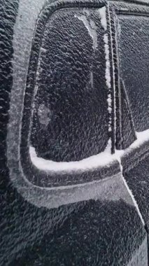 Dondurucu yağmur ve keskin sıcaklık düşüşünden sonra katı buzla kaplı siyah bir arabanın yakın çekim görüntüsü. Araç gövdesinde donmuş doku, kış havası çarpması, soğuk ve tehlikeli koşullar..