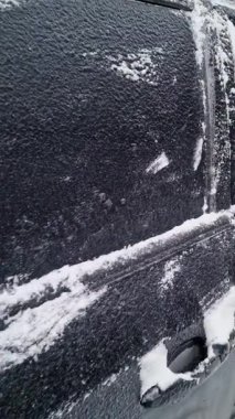 Dondurucu yağmurdan ve ani soğuktan sonra kalın buzla kaplı siyah bir arabanın yakın çekimi. Kış havası tehlikesi, aracın buzlu yüzeyi, kapılarda ve yan aynalarda donmuş detaylar, soğuk iklim.