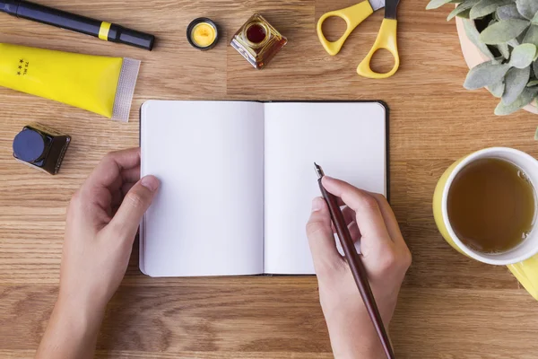 Χέρι με στυλό εγγράφως σχετικά με κενό σημειωματάριο και κίτρινο αντικείμενα — Φωτογραφία Αρχείου