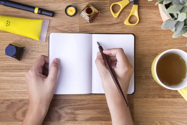 Χέρι με στυλό εγγράφως σχετικά με κενό σημειωματάριο και κίτρινο αντικείμενα — Φωτογραφία Αρχείου