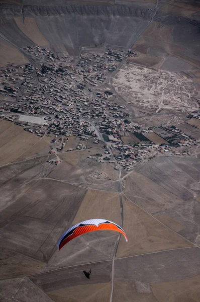 Parapente laranja e branco voando acima da aldeia — Fotografia de Stock