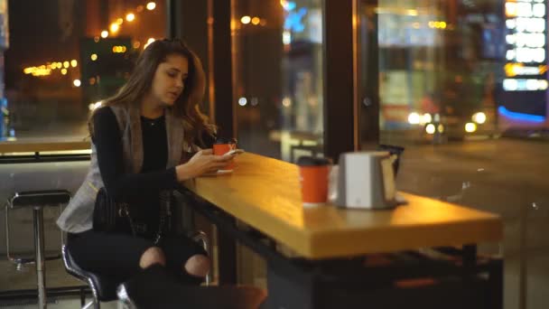 Девушка пьет кофе на заправке и пользуется телефоном — стоковое видео