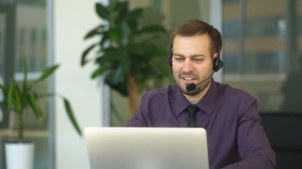 Un hombre sonriente con auriculares trabajando como operador de centro de llamadas — Vídeos de Stock