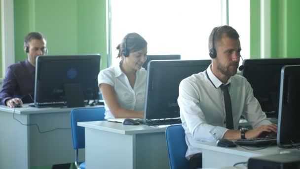 Colegas de negócios com fones de ouvido usando computadores na mesa do escritório m dern — Vídeo de Stock