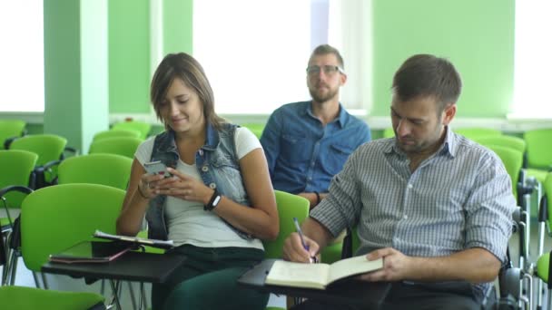 Lachende jonge mannelijke student met anderen schrijven nota's in de klas — Stockvideo