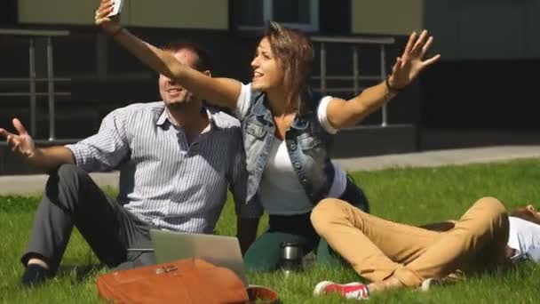 Группа счастливых друзей, делающих селфи на голубом небе на лужайке кампуса, белый — стоковое видео