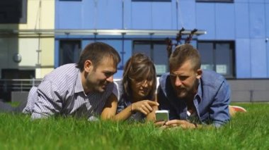 üç öğrenci kullanım telefon ve çim üzerinde yalan