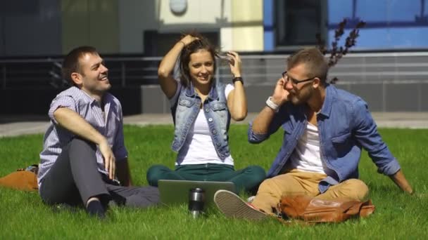 Drei Studenten sitzen auf dem Rasen in der Nähe der Universität und reden — Stockvideo