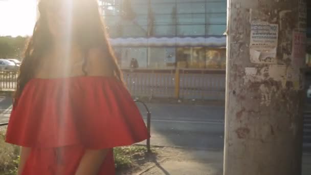 Красива дівчина в червоній сукні, що йде містом — стокове відео