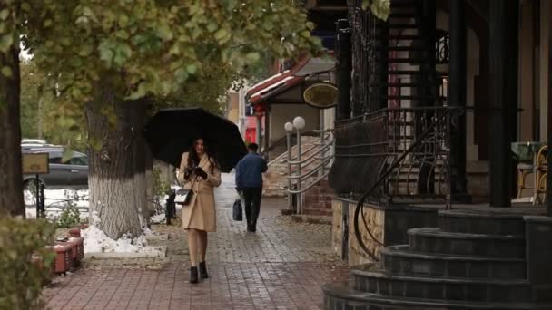 Girl under umbrella walking and typing a message — Stock Video