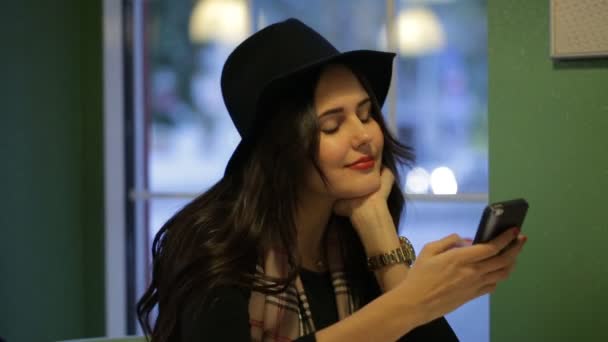 La chica sentada en la ventana de un café y escribe un mensaje — Vídeos de Stock