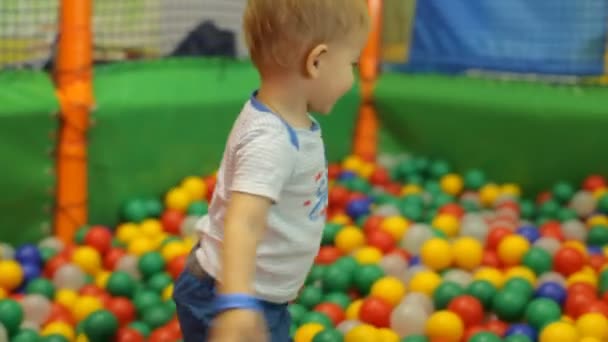 Kleiner lächelnder Junge spielt in bunten Bällen — Stockvideo