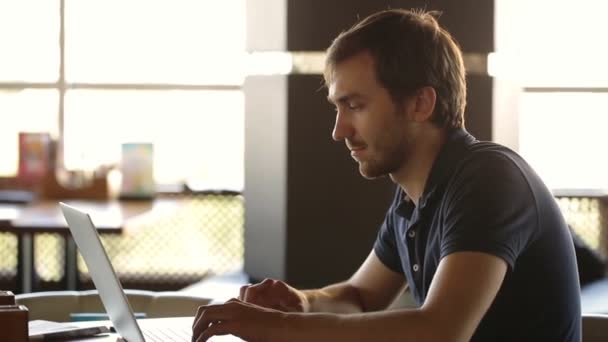 Ein Mann sitzt in einem Café und arbeitet an einem Laptop — Stockvideo