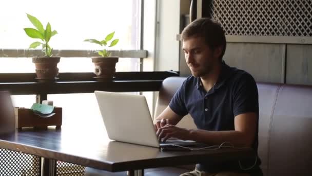 Ένας άνδρας κάθεται σε ένα καφέ και να εργάζονται σε ένα φορητό υπολογιστή — Αρχείο Βίντεο