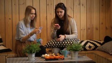güzel kızlar kafede çay ile oturup ve seyir akıllı telefon.