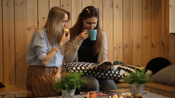 Dos chicas leyendo revista y oliendo en la cafetería — Vídeo de stock