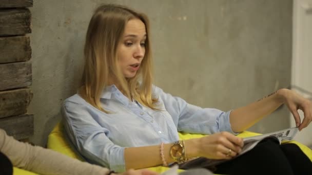 Hermosa chica hablando con su amigo y leyendo una revista — Vídeo de stock