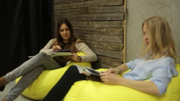 Två tjejer sitter och läser en tidning — Stockvideo
