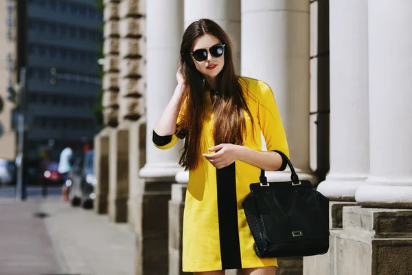 Retrato al aire libre de una joven hermosa dama caminando por la calle. Modelo con gafas de sol y elegante vestido de verano amarillo. Chica mirando hacia abajo. Concepto de moda femenina. Estilo de vida. Día soleado. Cintura para arriba — Foto de Stock