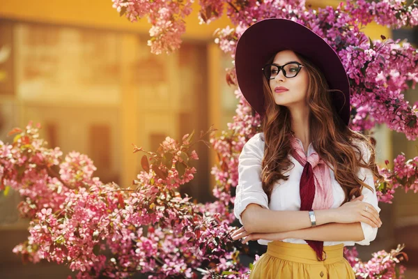 Outdoor portrait of young beautiful fashionable lady posing near flowering tree. Model wearing stylish accessories and clothes. Girl looking aside. Female beauty, fashion concept. City lifestyle. Copy — Stock Photo, Image