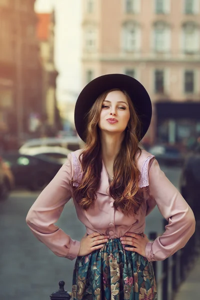 Outdoor portrait of young beautiful fashionable playful lady posing on old street. Model wearing stylish hat and clothes. Sunny day. Female fashion. City lifestyle. Toned style instagram filters — Stock Photo, Image