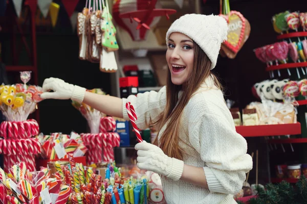 Street portrait of smiling beautiful young woman buying candy on the festive Christmas fair. Lady wearing classic stylish winter knitted clothes. Close up — Stock Photo, Image