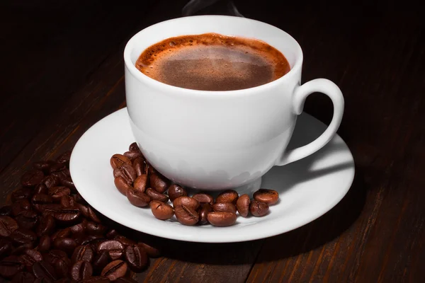 Taza de café blanco y granos de café en una mesa de madera. Fondo oscuro . — Foto de Stock