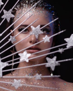 Parlak makyajlı ve süslemeli genç bir kız. Koyu arkaplanda yıldızlar olan bir taç..