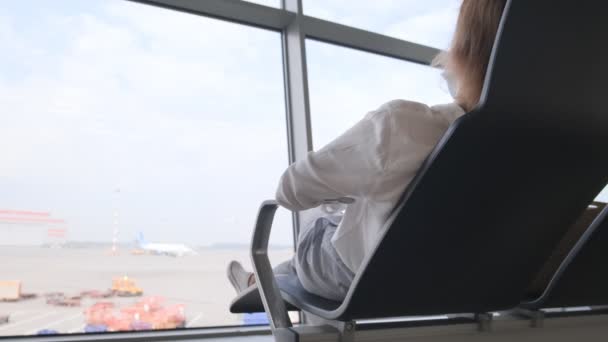 Женщина отдыхает в кресле в терминале аэропорта и ждет транзитного самолета — стоковое видео