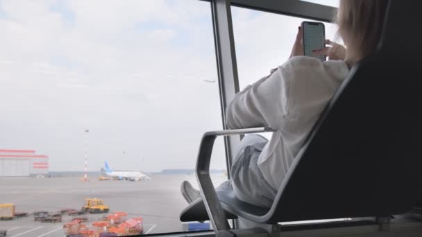 Wanita menggunakan telepon dan menunggu naik pesawat di terminal bandara — Stok Video