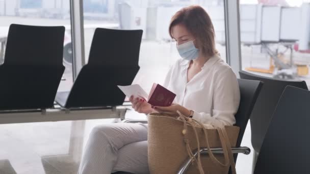 Vrouw met gezichtsmasker controleert paspoort en instapkaart in de terminal van de luchthaven — Stockvideo