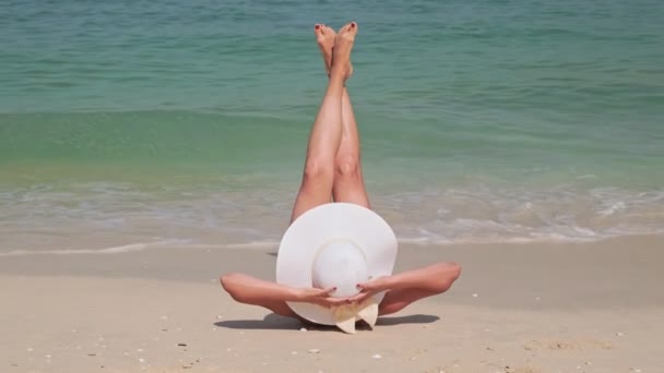 Mavi okyanus sörfüne karşı lüks bir tatil köyünde kumlu bir sahilde uzanan bir kız. — Stok video