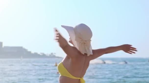 Gelukkige en vrolijke vrouw draaiend op het strand tegen blauwe zee en zonlicht — Stockvideo