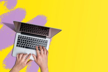 Renkli arkaplanda dizüstü bilgisayarlı eller üst görünümü olan boya darbeleriyle ve boşluğu kopyalayarak.