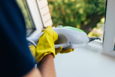 Kadın bir buhar cihazıyla pencereyi çamurdan temizliyor..