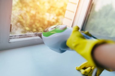 Bir insanın elindeki temizlik aleti pencerenin çerçevesine buhar püskürtür..