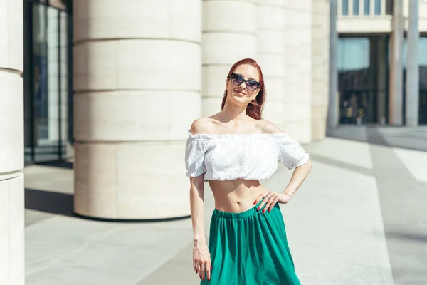 Fashionable woman in summer glasses posing at cameras on the background of a modern building.