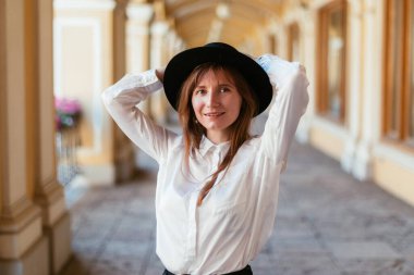 Şapkalı beyaz kız gülümsüyor ve şehirde dolaşıyor..