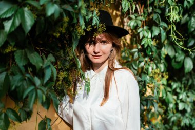 Kafkasyalı bir kız eski duvarın yanındaki yaprak sarkıtan kameraya bakıyor..