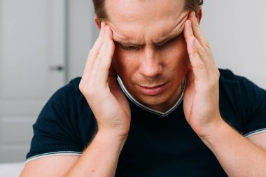 Beyaz bir adam evde oturuyor ve baş ağrısı çekiyor..