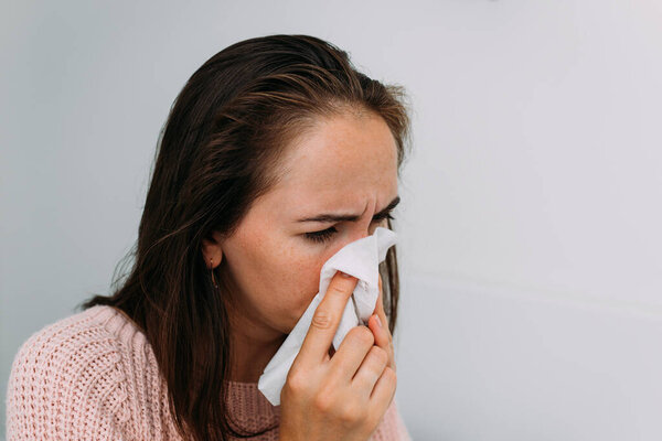 A Caucasian woman is sick with a cold and blows her nose into a handkerchief.
