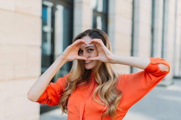 A woman of thirty from her hands makes a heart shape and looks in love — Stock Photo, Image