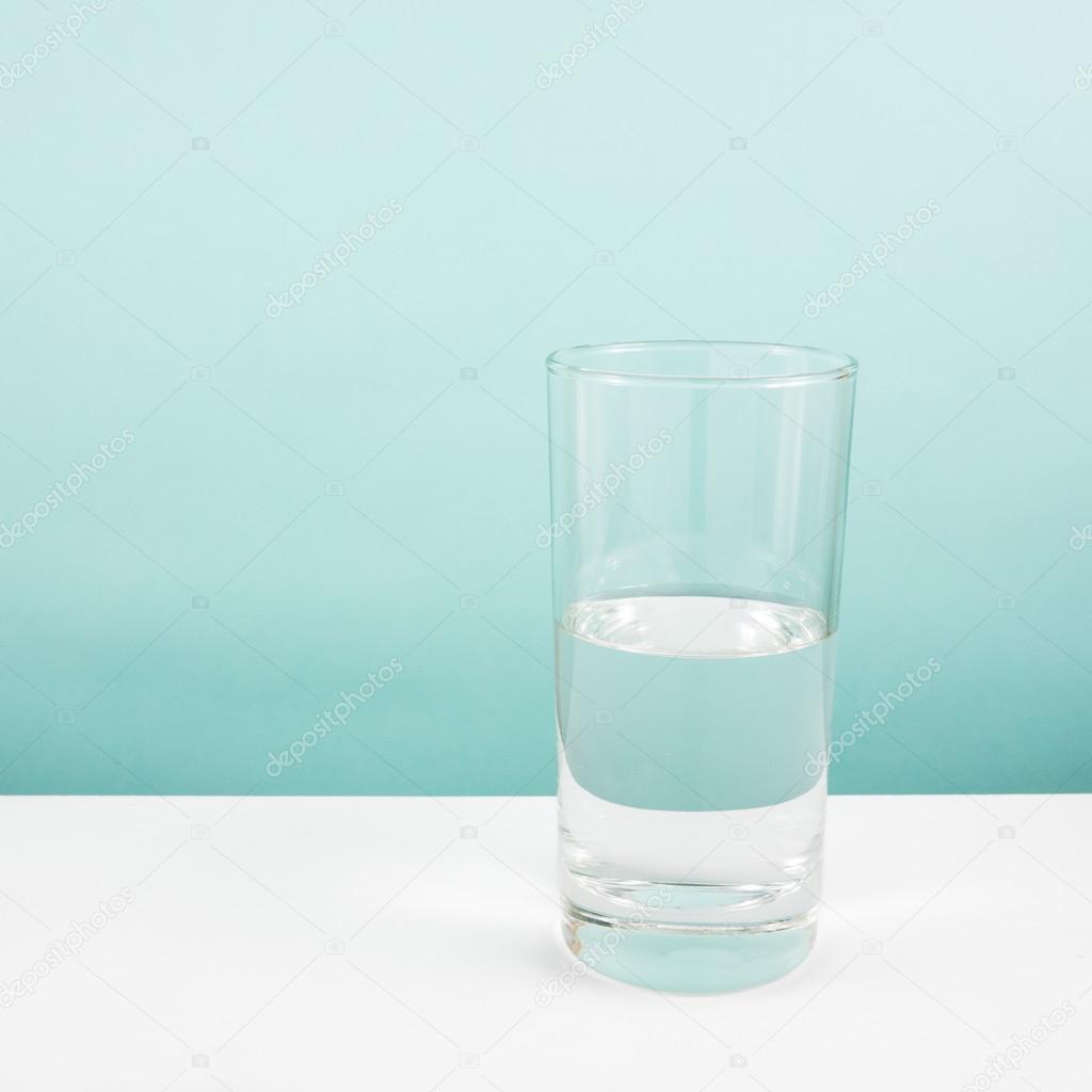 Half empty or half full glass of water on white table