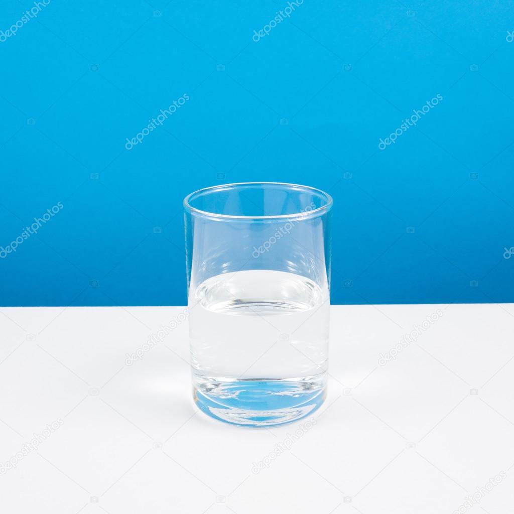 Half empty or half full glass of water on white table.
