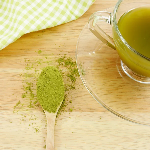 Japanese matcha green tea powder on the spoon and a cup of green tea on wooden board