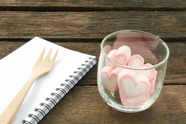 I deliziosi marshmallow cuore rosa in vetro rotondo e taccuino bianco con forchetta in legno — Foto Stock