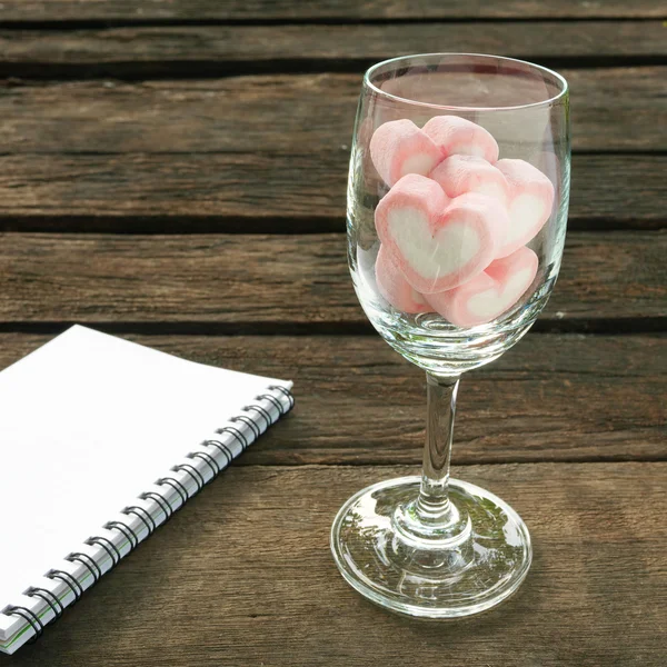 Il bel cuore rosa marshmallow in bicchiere di vino e libro di note bianche — Foto Stock