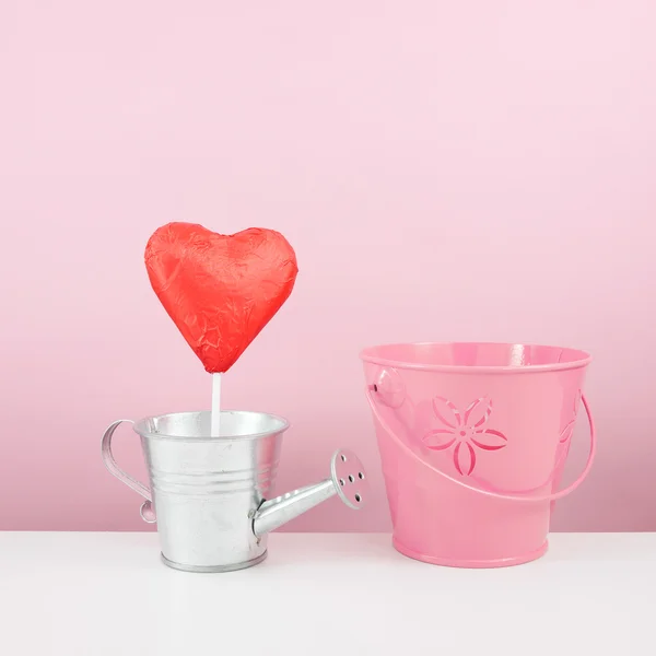 Il bastone di cuore di cioccolato sventato rosso con piccolo annaffiatoio d'argento e piccolo secchio rosa — Foto Stock