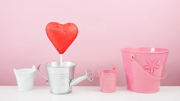 Il bastone di cuore di cioccolato sventato rosso con piccolo annaffiatoio d'argento e piccolo secchio rosa — Foto Stock